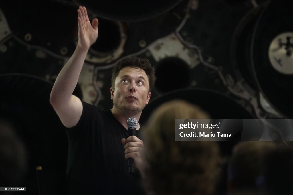 SpaceX CEO Elon Musk speaks in front of rocket components at a press