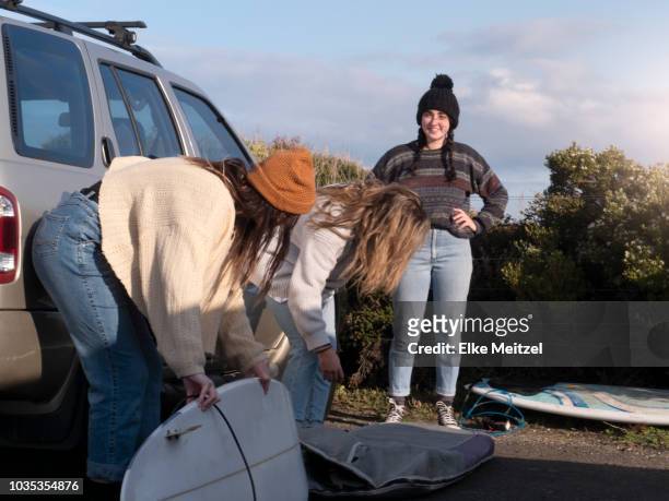 young women unloading surf boards from car - offloading stock-fotos und bilder