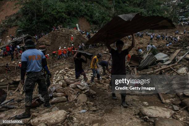 Workers carry metal debris as rescuers dig at the site where people were believed to have been buried by a landslide on September 18, 2018 in in...