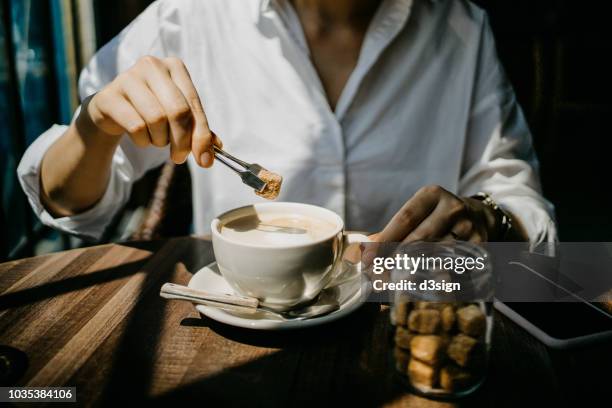 woman putting brown sugar cube into coffee and ready to enjoy it on a fresh morning - brown sugar stock pictures, royalty-free photos & images