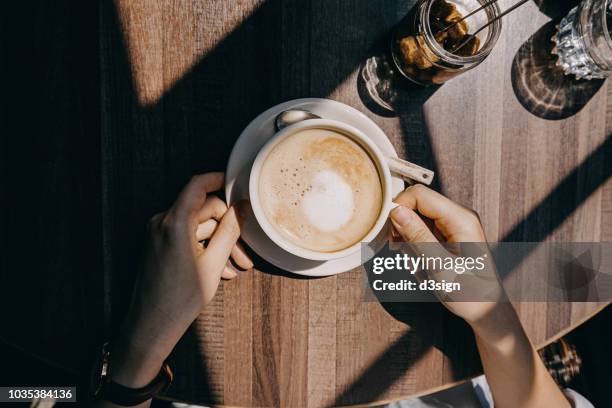 top view of woman sitting by the window in coffee shop enjoying the warmth of sunlight and drinking coffee - café stockfoto's en -beelden