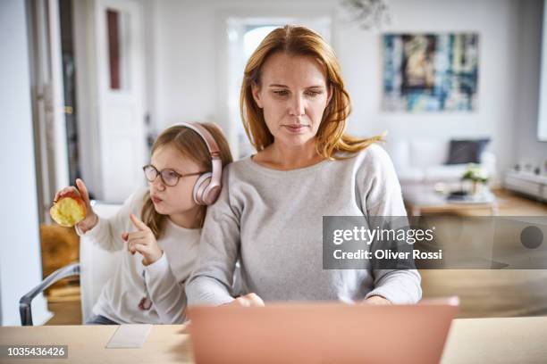 woman using laptop with daughter listening to music on headphones at home - working from home kids stock pictures, royalty-free photos & images
