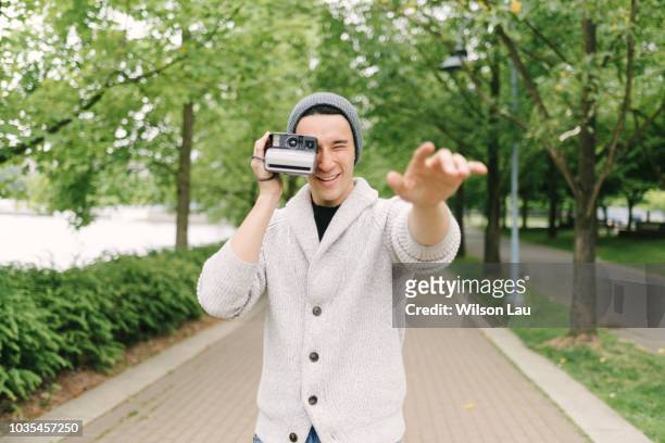 young man taking photo with instant camera, vancouver, canada - pointing at camera - fotografias e filmes do acervo