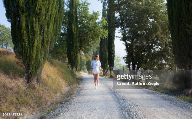 woman walking on tuscan country road in the morning light - toscana stock-fotos und bilder