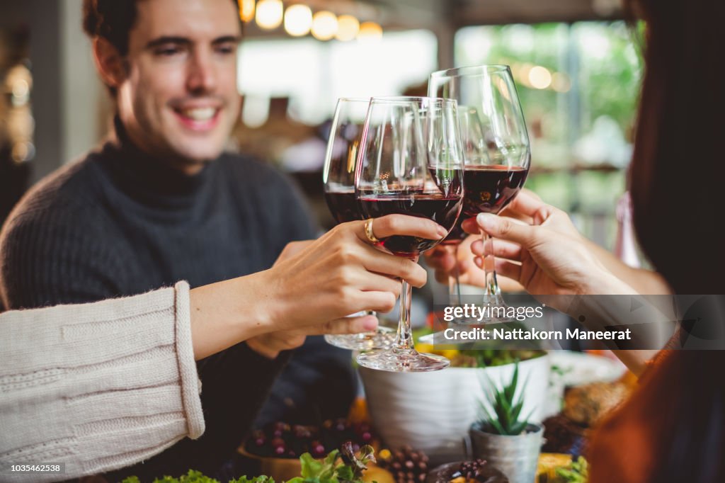 Group of young people celebrating Christmas party dinner with clinking glass of wine