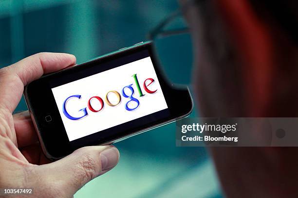 Businessman checks the Google Inc company logo displayed on the screen of Apple Inc.'s Apple iPhone in an arranged photograph in London, U.K., on...