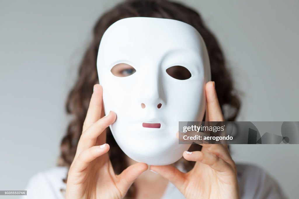 Nahaufnahme Porträt einer Frau, die Maske vor weißem Hintergrund hält