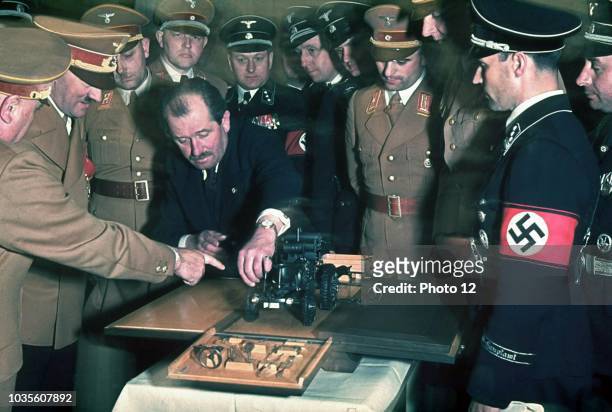 Colour photograph of the automobile engineer and designer Ferdinand Porsche presents Adolf Hitler with a model car during celebrations for Hitler's...