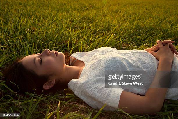 young asian woman lying in grass at sunset - west asia stock-fotos und bilder
