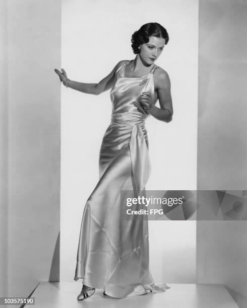 Actress and dancer Eleanor Powell pictured wearing a white satin formal gown, USA, circa 1935. The gown features a double rhinestone band with the...