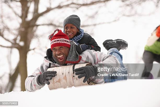 african american father and son sledding on snowy hill - day toronto stockfoto's en -beelden