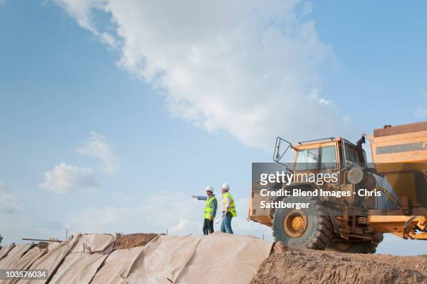 hispanic construction workers in field with dump truck - maquinaria de construcción fotografías e imágenes de stock