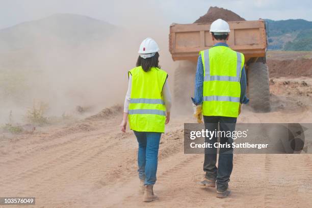 construction workers walking behind dump truck - leuchtbekleidung stock-fotos und bilder