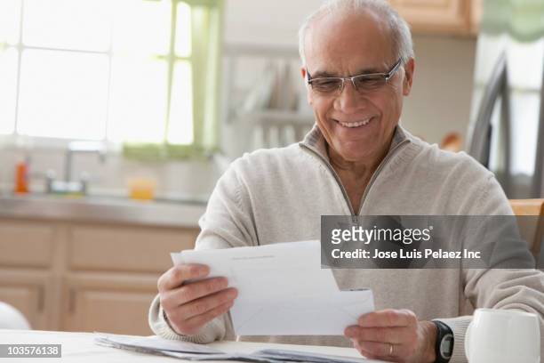 hispanic man reading mail in kitchen - rentner mann allein lustig stock-fotos und bilder