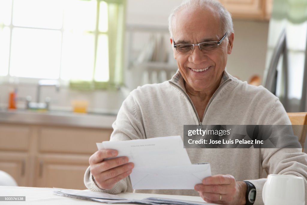 Hispanic man reading mail in kitchen