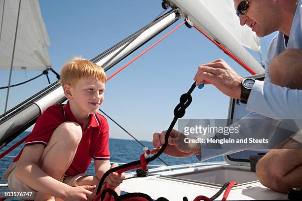 man teaching boy knot on yacht - knoten stock-fotos und bilder