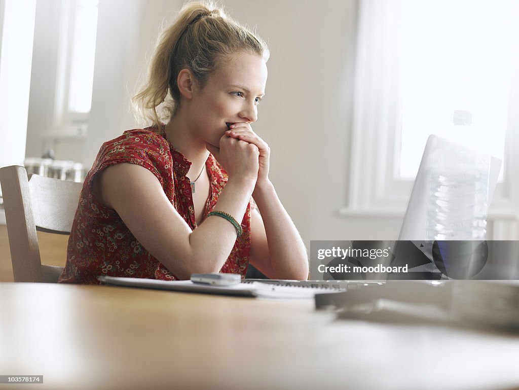 Woman using laptop sitting at dining table, low angle view