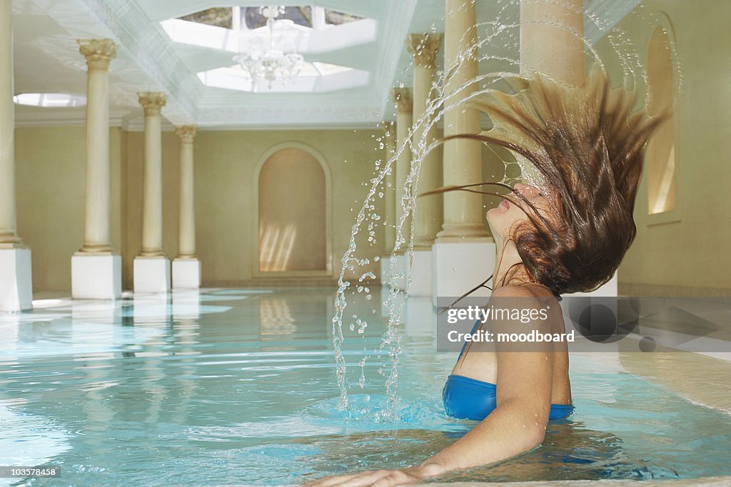 Young woman throwing wet hair back in swimming pool, side view