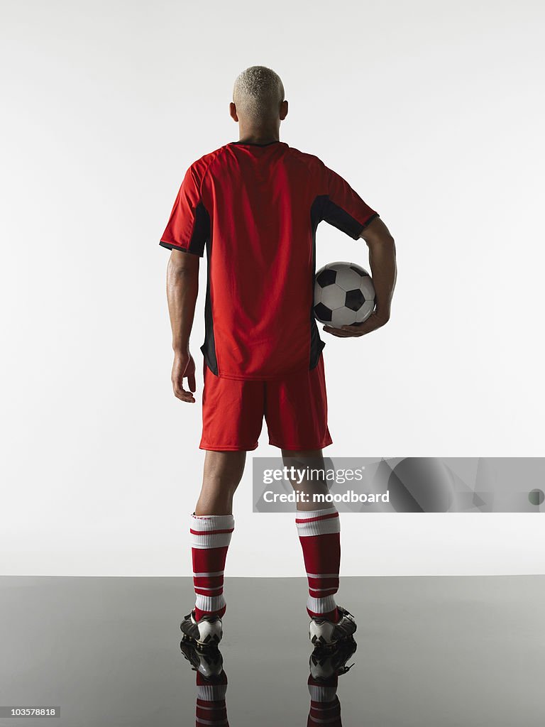 Football player standing holding ball, back view