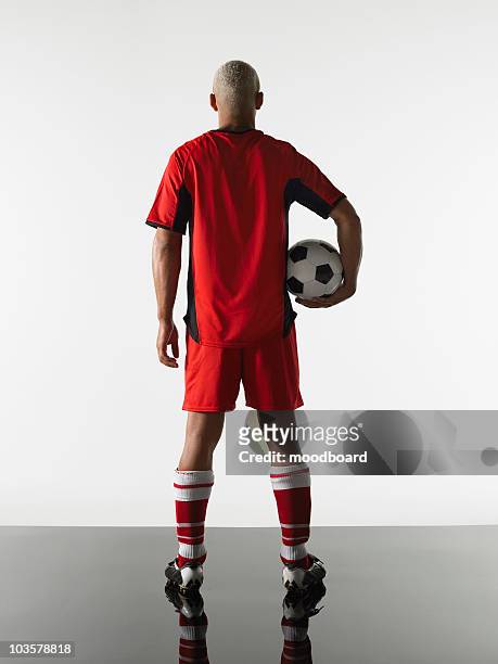football player standing holding ball, back view - soccer back stock-fotos und bilder