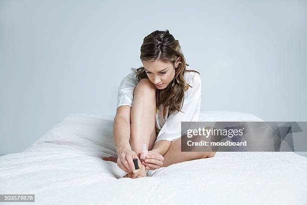 young woman painting toe nails on bed - painting toenails stock-fotos und bilder