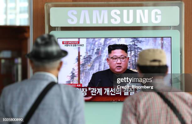 Two men watch a television screen showing a broadcast, featuring North Korean leader Kim Jong-un attending a news conference with South Korean...