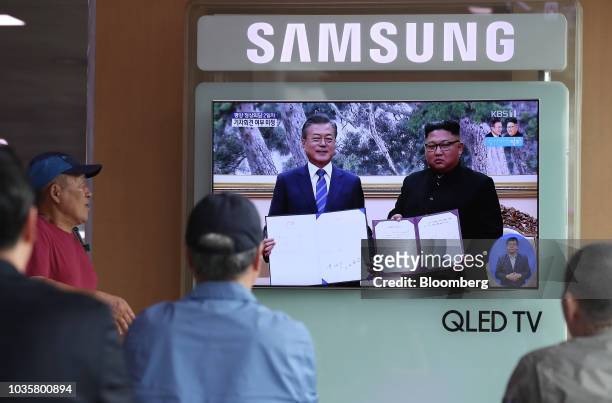 People watch a television screen showing a broadcast, featuring South Korean President Moon Jae-in, left, and North Korean leader Kim Jong-un...