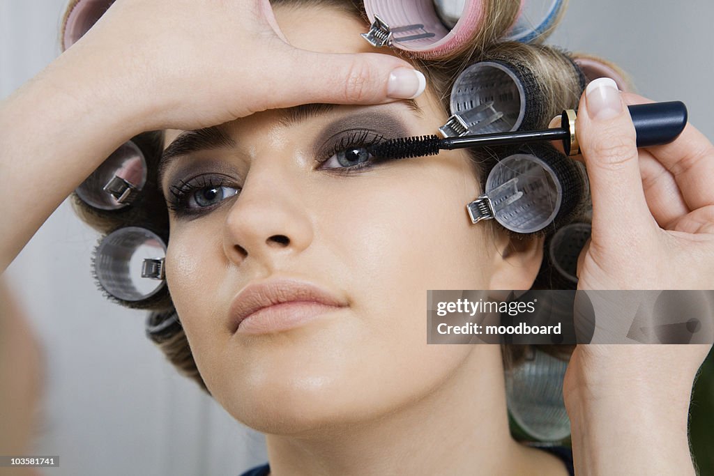 Model in Hair Curlers Having Makeup Applied