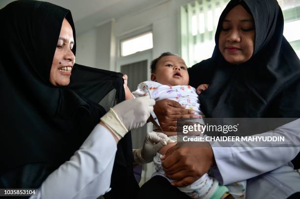 Medical worker injects a baby with a measles-rubella vaccine at a health station in Banda Aceh in Aceh province on September 19, 2018. - The acting...