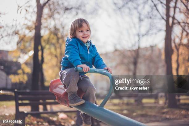 cute little boy on seesaw is enjoying at playground during autumn day. - see saw stock pictures, royalty-free photos & images