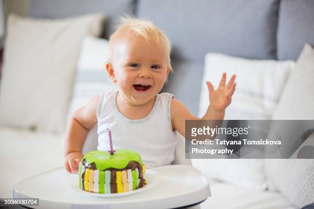 little baby boy, eating cake for his first birthday in high chair at home - eerste verjaardag stockfoto's en -beelden