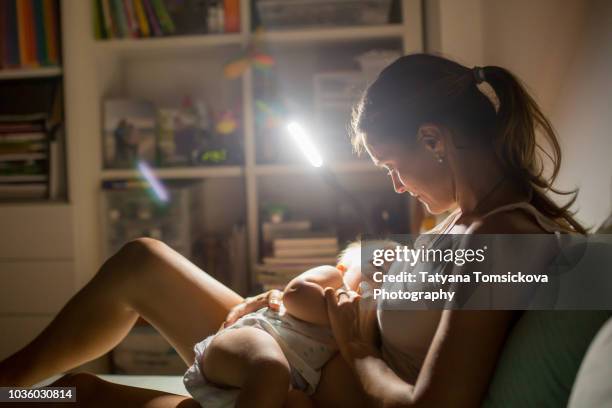 young beautiful mother breastfeeding her newborn baby boy at night dim light. mom breastfeeding infant - dark baby stock pictures, royalty-free photos & images