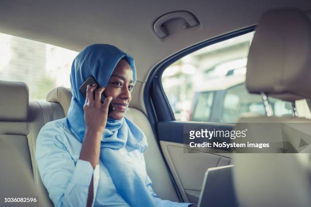 eine muslimische geschäftsfrau in ein taxi, mit laptop und handy - fachmann auto smartphone stock-fotos und bilder