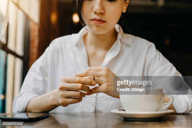 woman touching the wedding ring on her finger nervously while having coffee and waiting in cafe - promesas de matrimonio fotografías e imágenes de stock