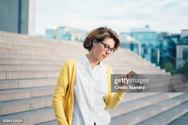 kaukasische vrouw met behulp van smartphone buitenshuis - mid volwassen vrouw stockfoto's en -beelden