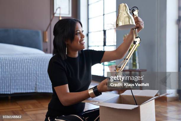 young woman opening box with lamp at home - electric lamp stock pictures, royalty-free photos & images