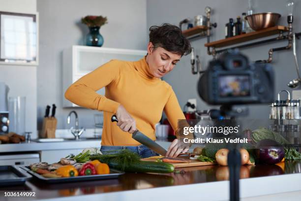 female food vlogger making video while prepping vegetables in kitchen - camera woman stock-fotos und bilder