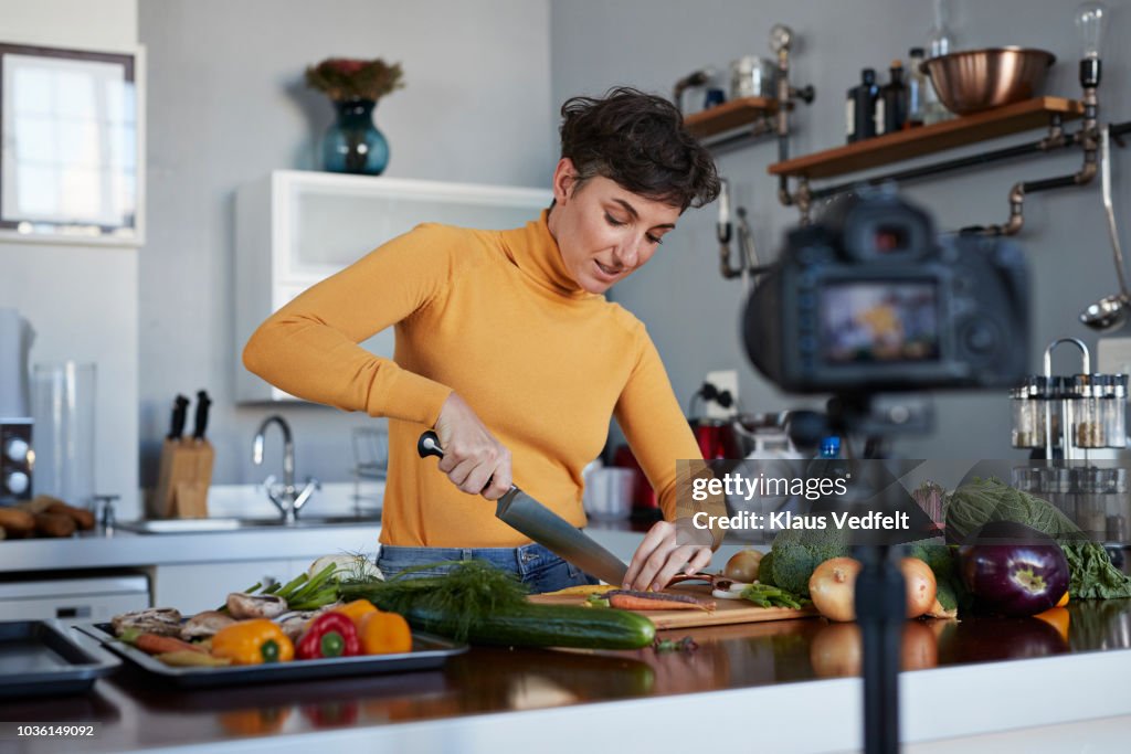 Female food vlogger making video while prepping vegetables in kitchen