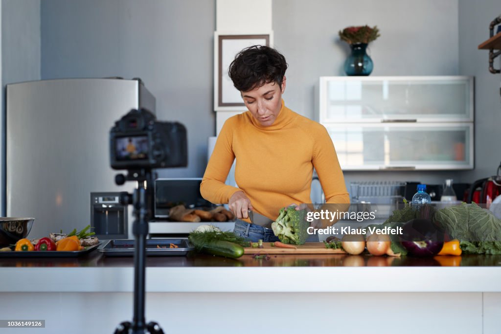 Female food vlogger making video while prepping vegetables in kitchen