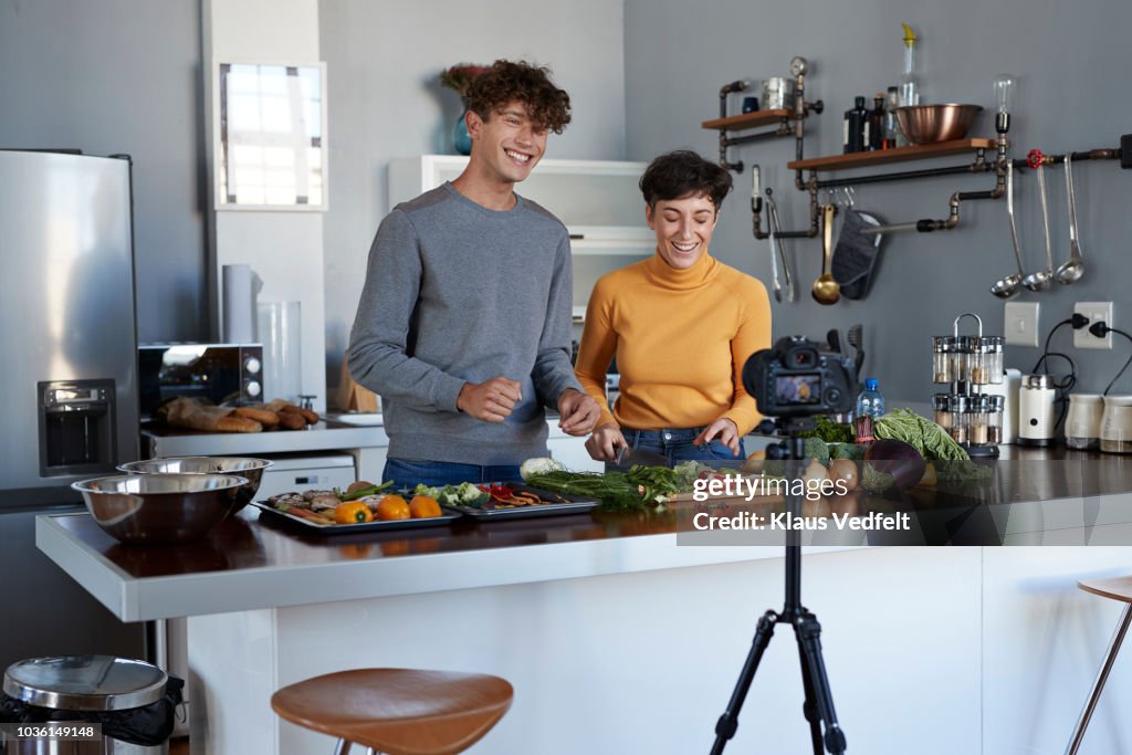 Two food vloggers making video while prepping vegetables in kitchen