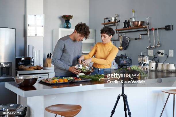 two food vloggers making video while prepping vegetables in kitchen - creative collaboration holding stockfoto's en -beelden