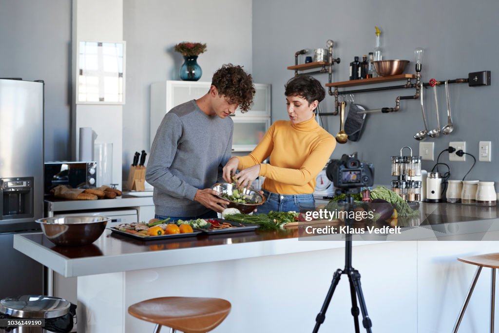 Two food vloggers making video while prepping vegetables in kitchen