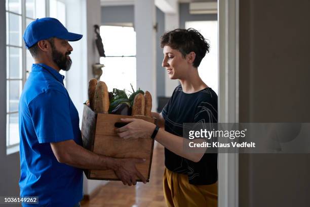 woman receiving groceries from delivery person - gemüsekiste stock-fotos und bilder