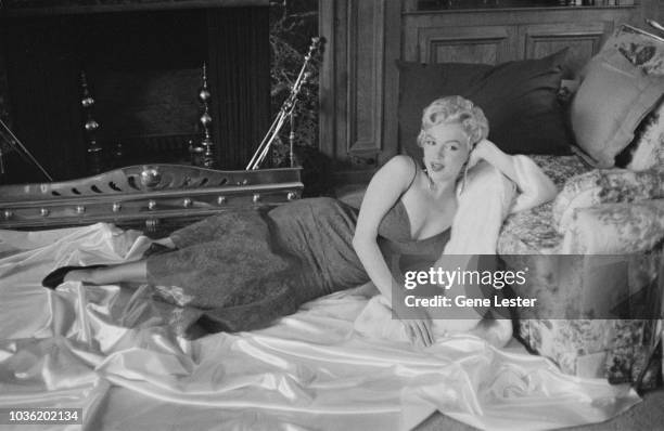 American actress Marilyn Monroe reclining on white satin in a brocade evening gown, 1955.