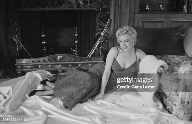 American actress Marilyn Monroe reclining on white satin in a brocade evening gown, 1955.