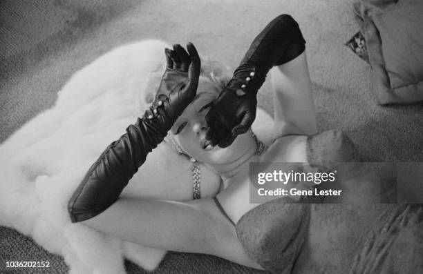 American actress Marilyn Monroe wearing a brocade evening gown and black evening gloves, and lying with her head resting on a white fur coat, 1955.