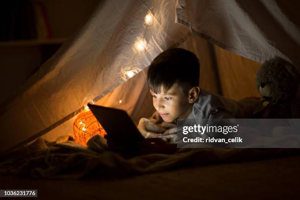 little boy reading book on digital tablet at night - boy using ipad stock pictures, royalty-free photos & images