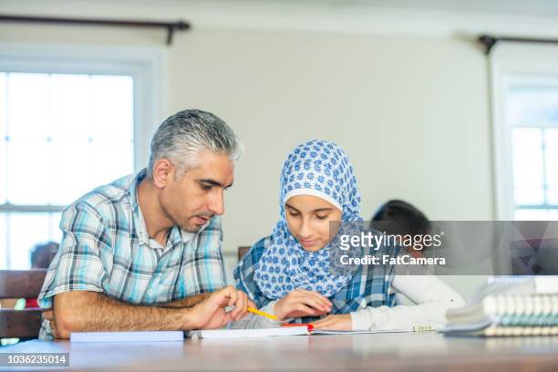 father shows his muslim daughter how to read and write in their home - english language stock pictures, royalty-free photos & images