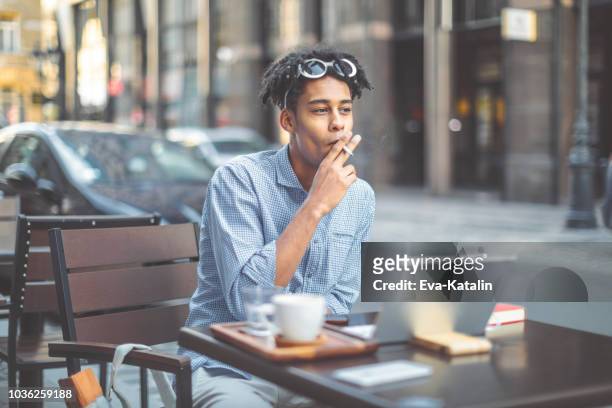 hipster is smoking a cigarette in a sidewalk cafe - smoking issues stock pictures, royalty-free photos & images