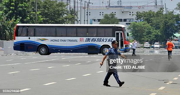 Policeman walks in front of a tourist bus while two negotiators walk towards the bus after an ex-policeman armed with a high-powered assault rifle...